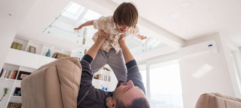Un papà gioca col figlio in un soggiorno raffrescato da un condizionatore