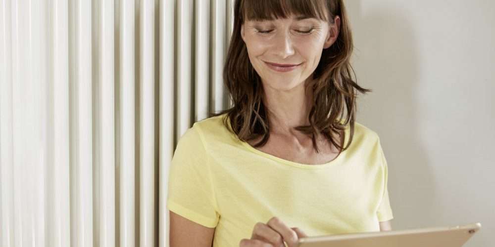 Una ragazza accanto a un termosifone regola la temperatura da remoto, funzione disponibile grazie alla domotica