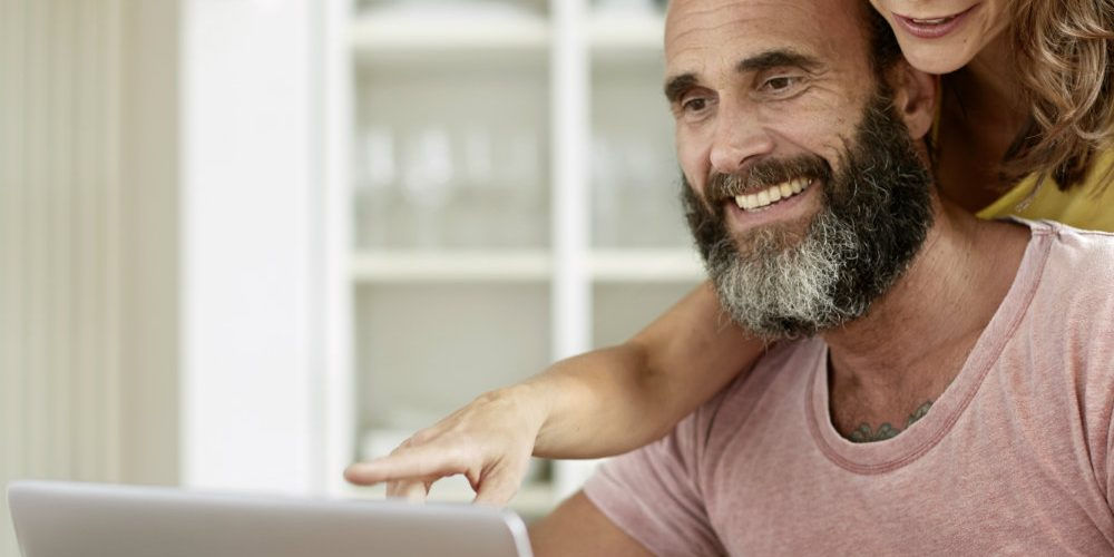 Una coppia sorridente davanti al computer: anche con i pc possiamo ridurre il consumo di energia e risparmiare