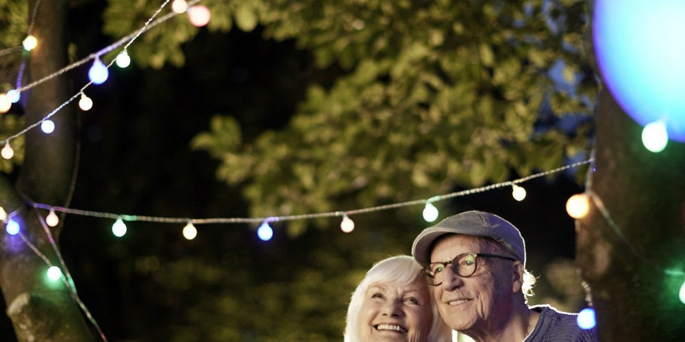 Una coppia di anziani sorridenti sotto una fila di luci all’aperto: per richieste contenute di watt esistono modi alternativi per produrre elettricità