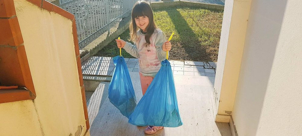 Una bambina con due sacchi di immondizia: l’educazione ambientale può essere insegnata come un gioco
