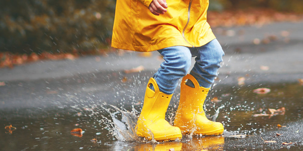 Un bambino con impermeabile e stivali di gomma gialli gioca con una pozzanghera in una mite giornata invernale