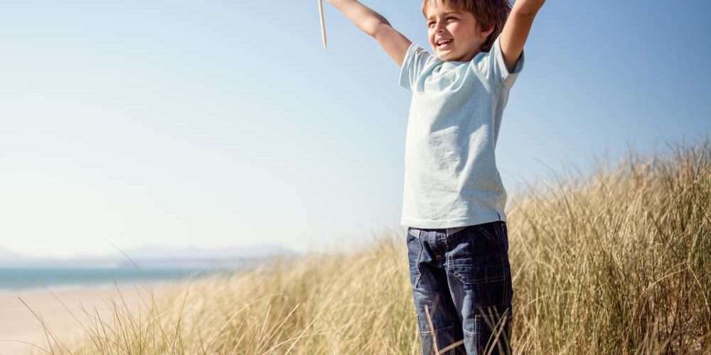 Un bambino con le braccia alzate sul prato vicino alla spiaggia sorride durante una giornata di sole