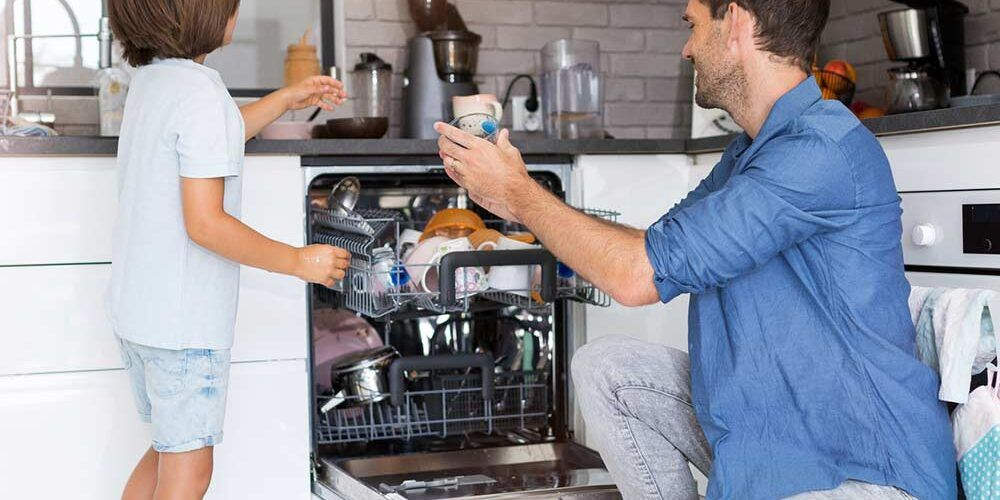 Un papà e un bambino riempiono una lavastoviglie rigenerata, esempio di economia circolare