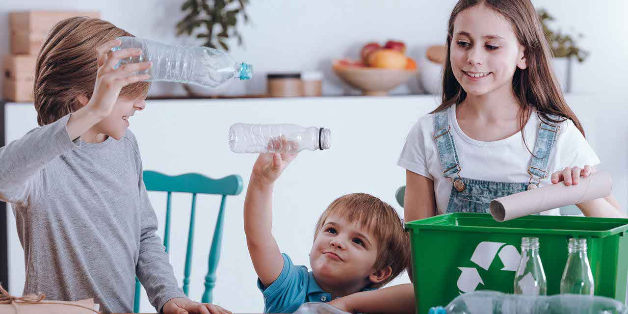 Tre bambini sistemano in contenitori bottiglie di plastica vuote da riciclare o riutilizzare