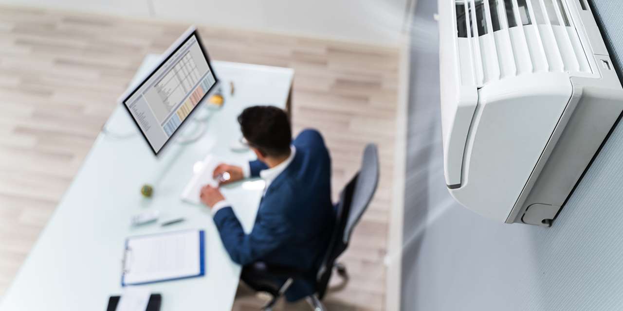Un uomo al computer al lavoro in uno studio con un condizionatore con inverter alle sue spalle