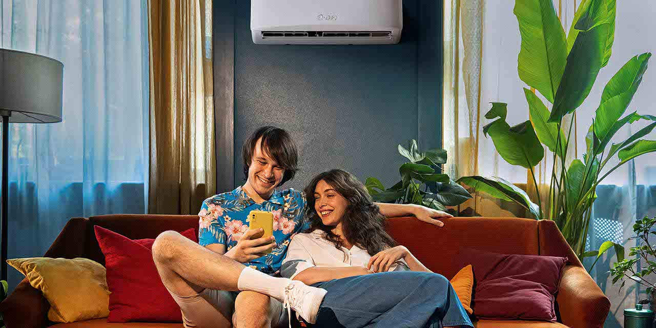 Una giovane coppia su un divano regola il climatizzatore con lo smartphone