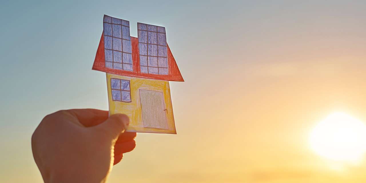 Una mano di un bambino solleva verso il cielo una casa di carta ritagliata, colorata e con celle solari sul tetto