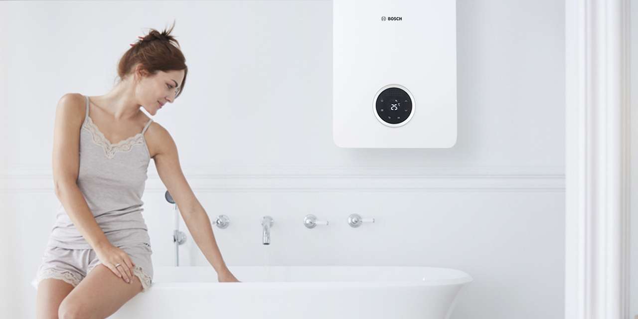 Una ragazza seduta sul bordo di una vasca controlla la temperatura dell’acqua riscaldata da uno scaldabagno