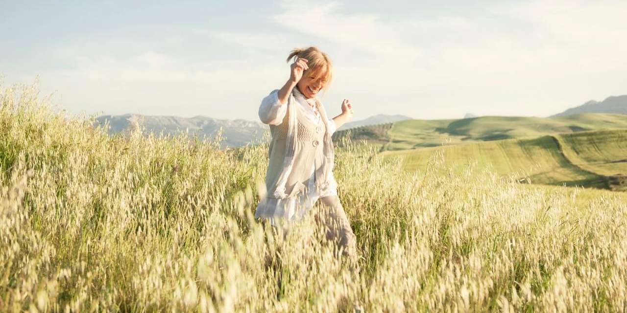 Una donna corre felice in un campo: tutti possiamo migliorare la nostra impronta ecologica