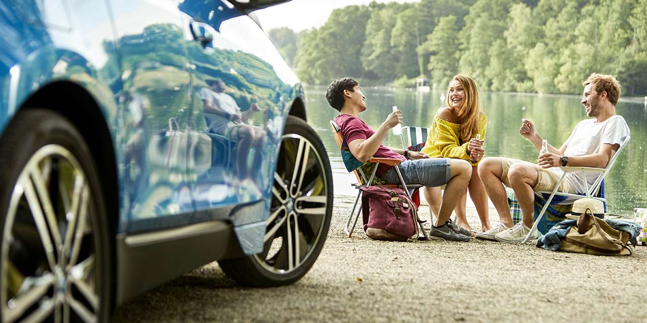 Una ragazza e due ragazzi seduti accanto a un lago: conoscere tutto sula ricarica elettrica è fondamentale per viaggi fuori porta