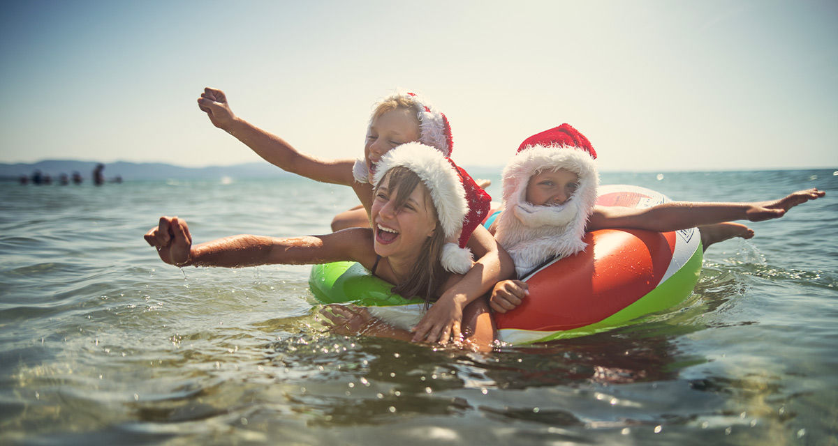 Dei bambini con i cappelli natalizi fanno il bagno al mare: uno scenario che il cambiamento climatico renderà possibile non solo nell’emisfero australe