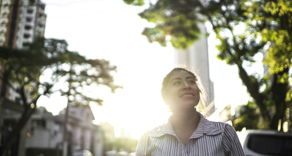 Una ragazza sorridente cammina in città con alle spalle il sole, l’energia rinnovabile per eccellenza per la transizione energetica