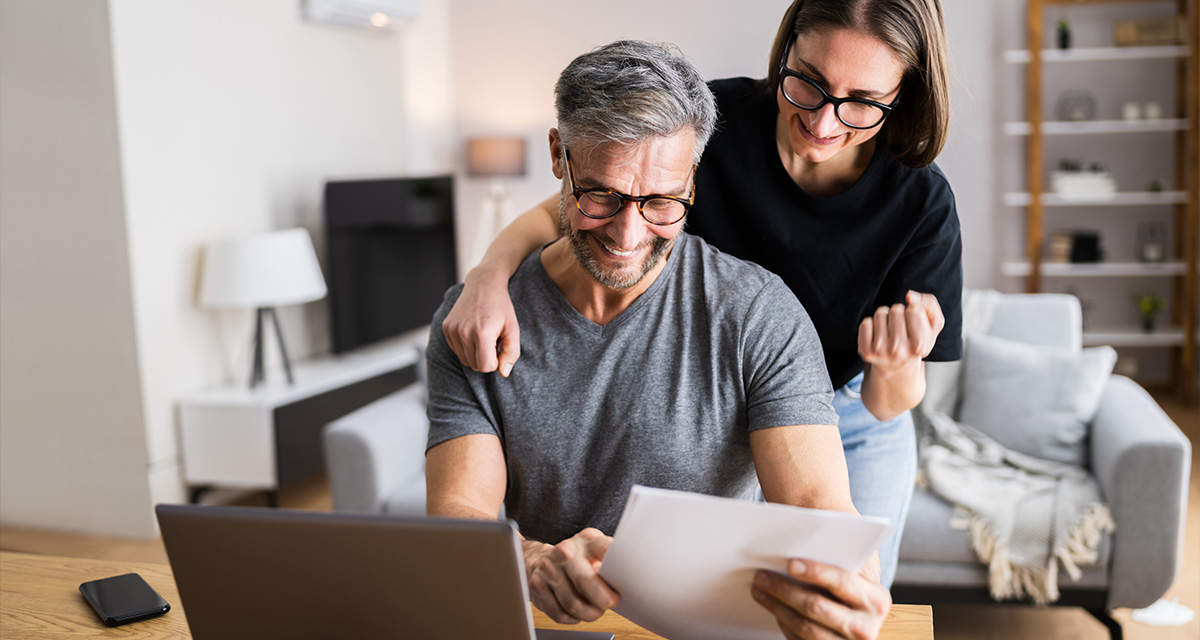 Una coppia sorride mentre consulta dei documenti davanti a un portatile.