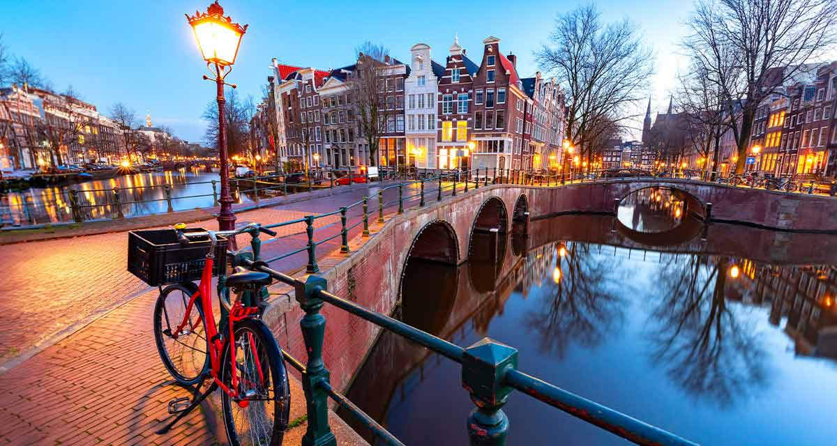 Una bicicletta è appoggiata alla ringhiera di un ponte, accanto a un lampione, su un canale cittadino: anche le città dovranno adattarsi ai cambiamenti climatici