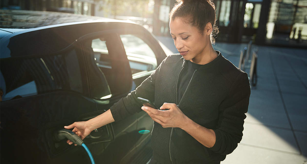 Una ragazza controlla lo smartphone mentre ricarica la batteria dell’auto elettrica