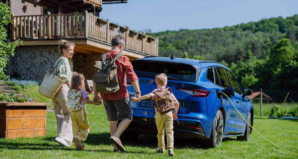 Una famiglia di quattro persone, camminando su un prato, si avvia a prendere la propria auto elettrica in carica