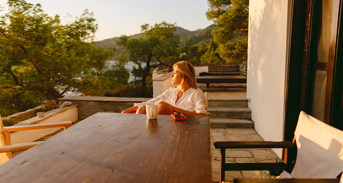Una ragazza seduta a un tavolo di legno si rilassa nella luce del tramonto su una terrazza vista mare