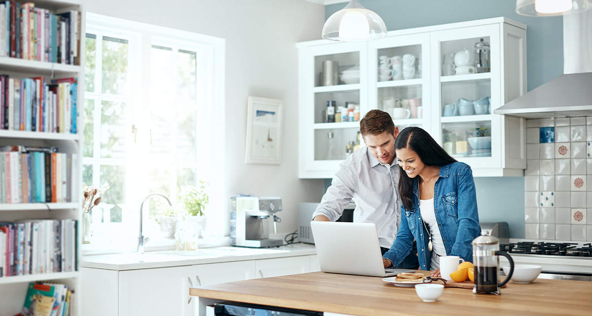 Una giovane coppia sorridente controlla un laptop sul tavolo di una cucina