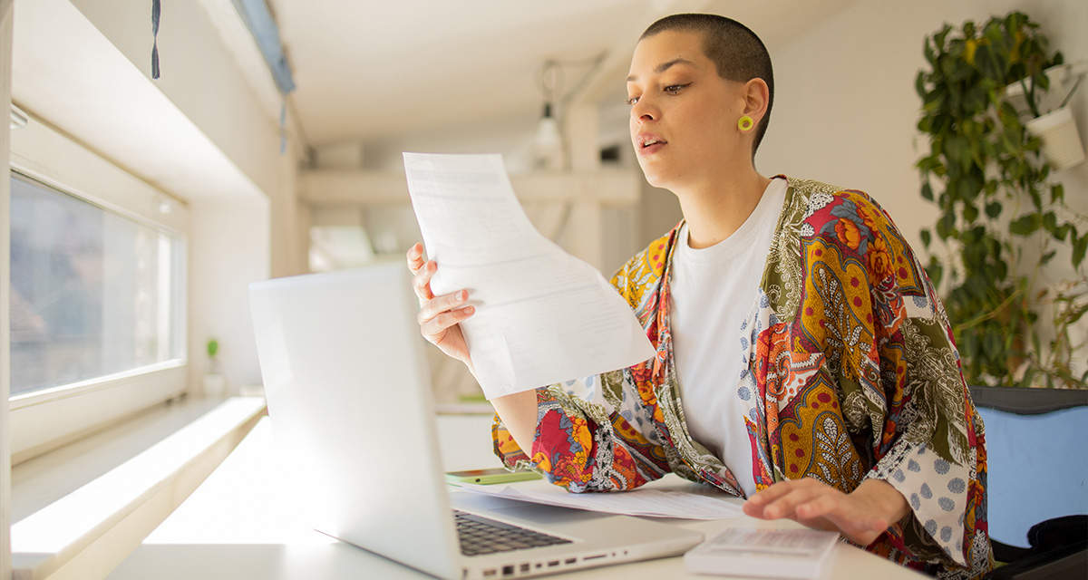 Una ragazza seduta a una scrivania in un soggiorno illuminato dal sole legge una bolletta della luce