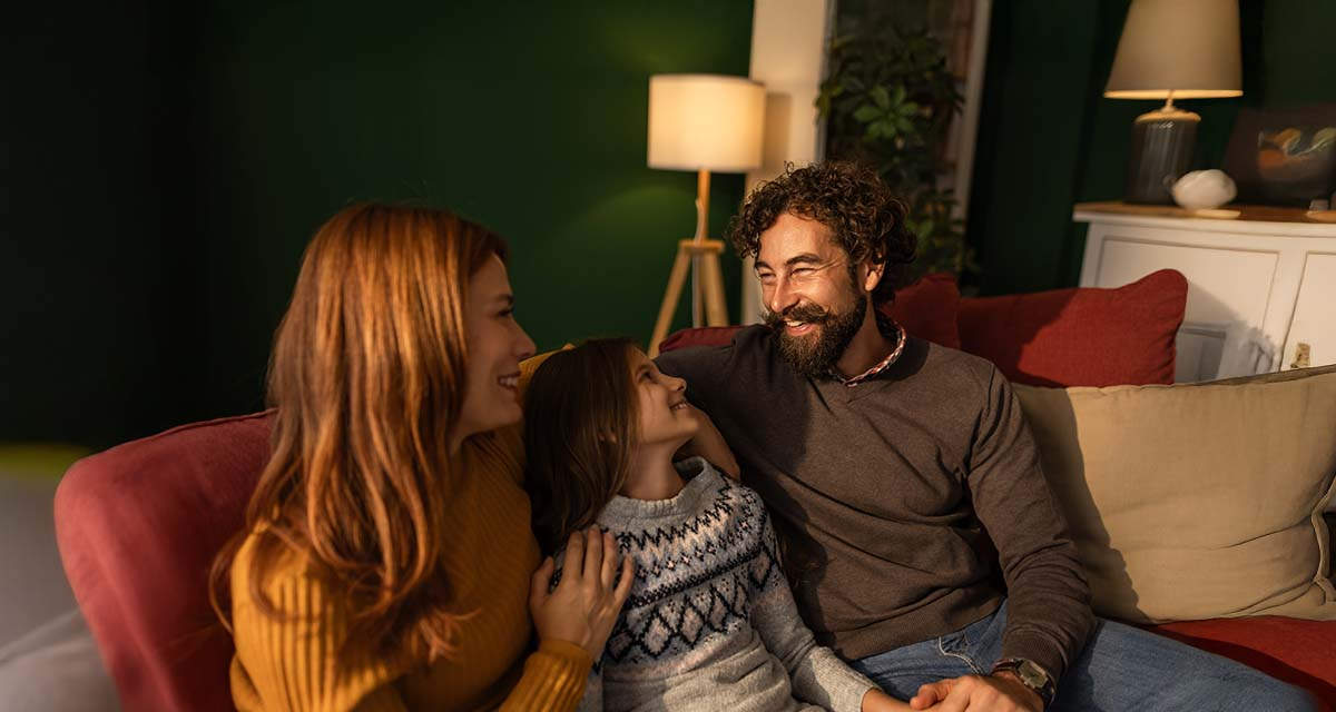 Una famiglia si rilassa su un divano in soggiorno: le soluzioni di riscaldamento sostenibile rendono più piacevole il clima domestico